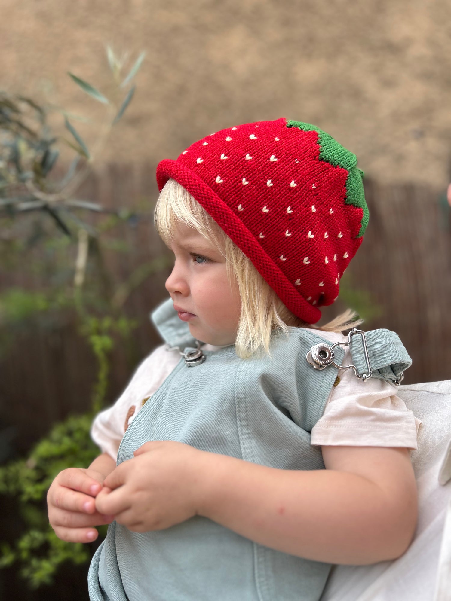 Child wearing a red strawberry knit hat outdoors