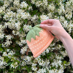 Hand holding a knitted strawberry hat against a white jasmin background