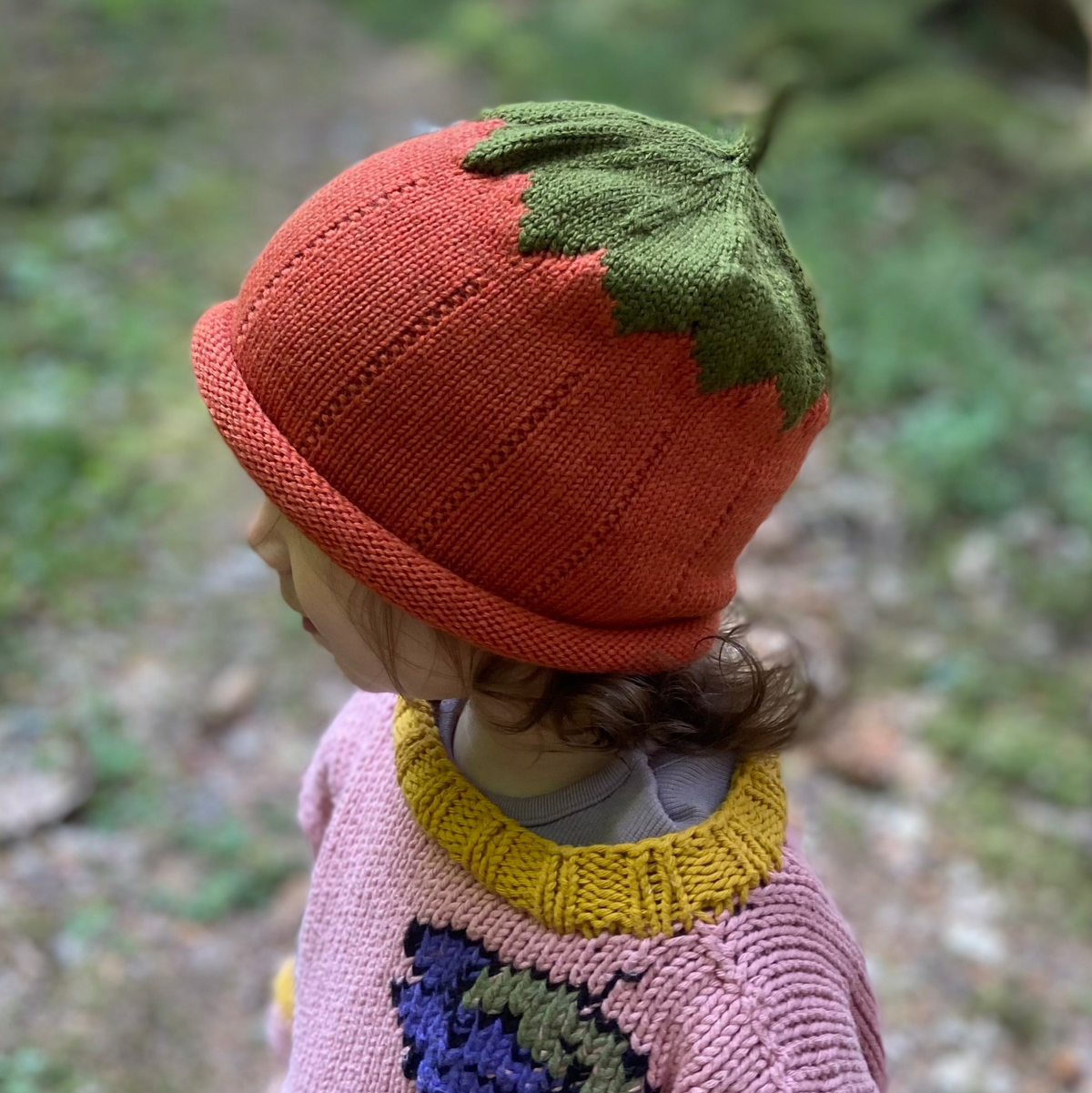 Child wearing a pumkin hat in a forest setting