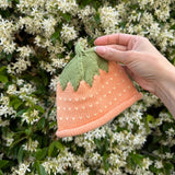 Hand holding a knitted strawberry hat against a floral background