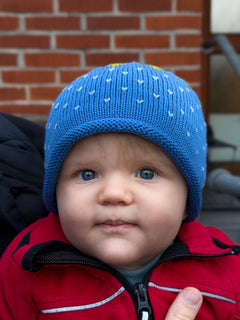 Child wearing a blue knit hat with white patterns against a brick wall.