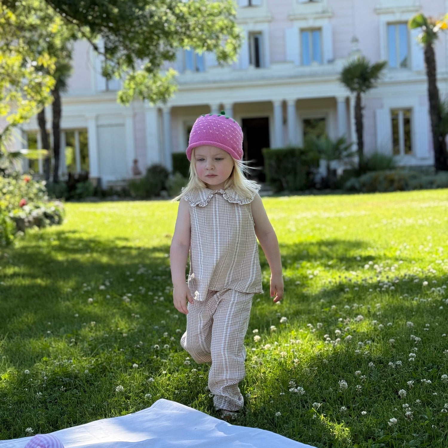 Child in a pink hat standing on grass in front of a large building