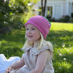 Child wearing a pink hat sitting on a blanket in a garden