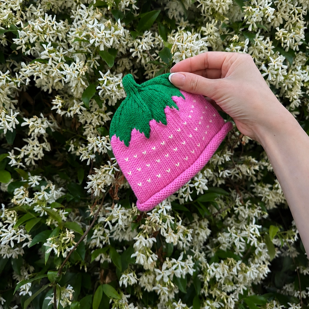 Hand holding a pink and green knitted strawberry-shaped object against a floral background