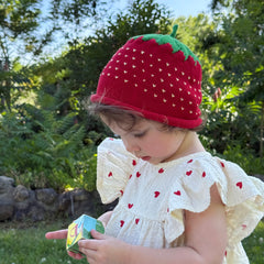 Child wearing a strawberry hat and dress with heart patterns outdoors