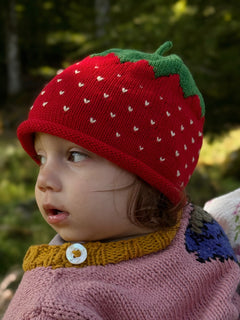 Child wearing a red strawberry knit hat outdoors