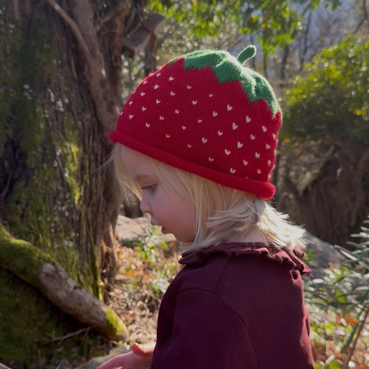 Child wearing a red strawberry hat in a natural setting